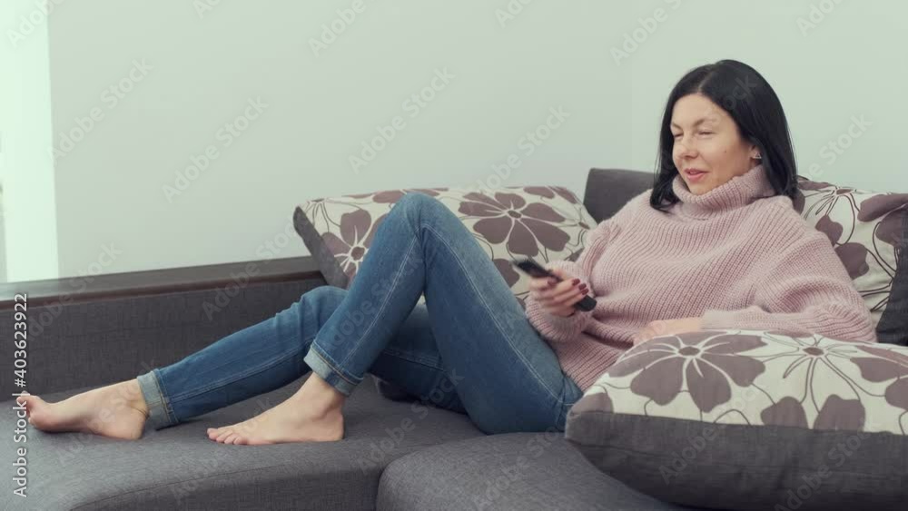 cheerful woman sitting on a sofa with a TV remote control in her hands and switching channels. cheerful woman sitting on a sofa with a TV remote control in her hands and switching channels.