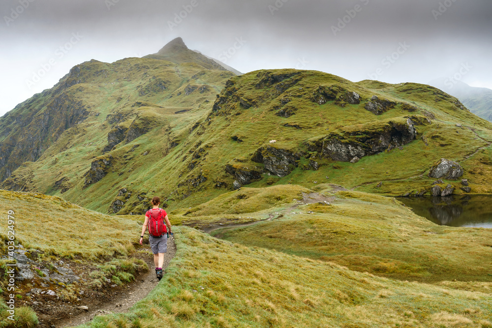 An active female hiker walking down from Meall nan Tarmachan towards Meall Garbh near Loch Tay in the Scottish Highlands, UK hiking.