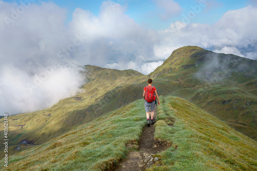 A female hiker walking over the narrow mountain ridge of the summit of Meall Garbh towards Beinn Nan Eachan near Loch Tay in the Scottish Highlands  UK mountains.