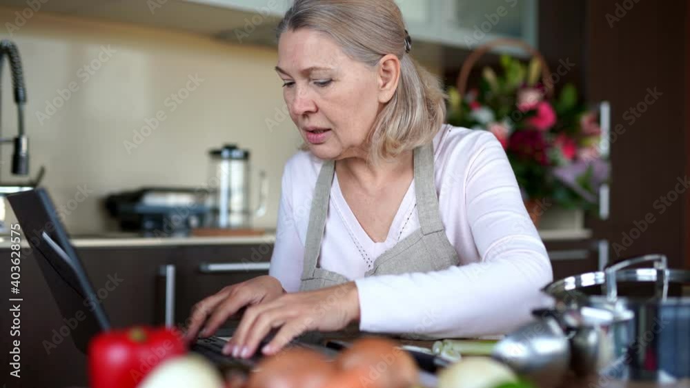Senior woman cooking with help of recipe on laptop Senior woman cooking with help of recipe on laptop