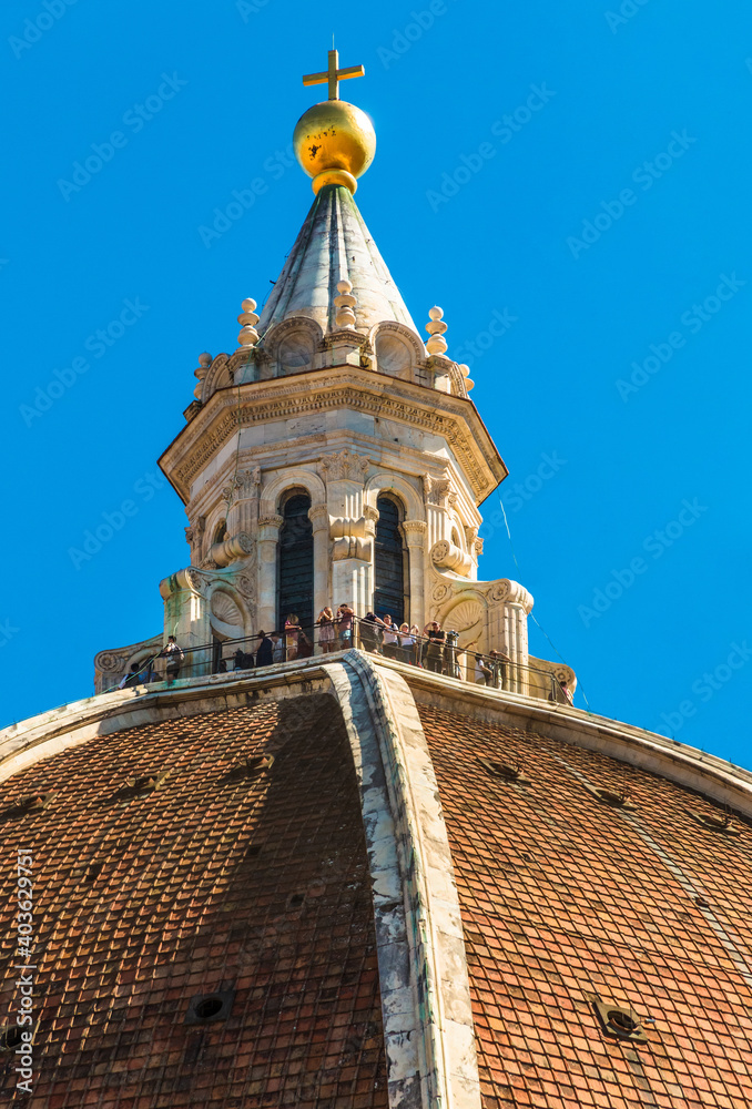 Gorgeous close-up view of people standing on the cupola on top of the Basilica's dome Santa Maria del Fiore, enjoying the view over Florence. The cupola is crowned with a gilt copper ball and cross.
