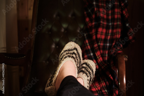Outstretched legs in knitted socks on a blurred background of an armchair with a checkered plaid.