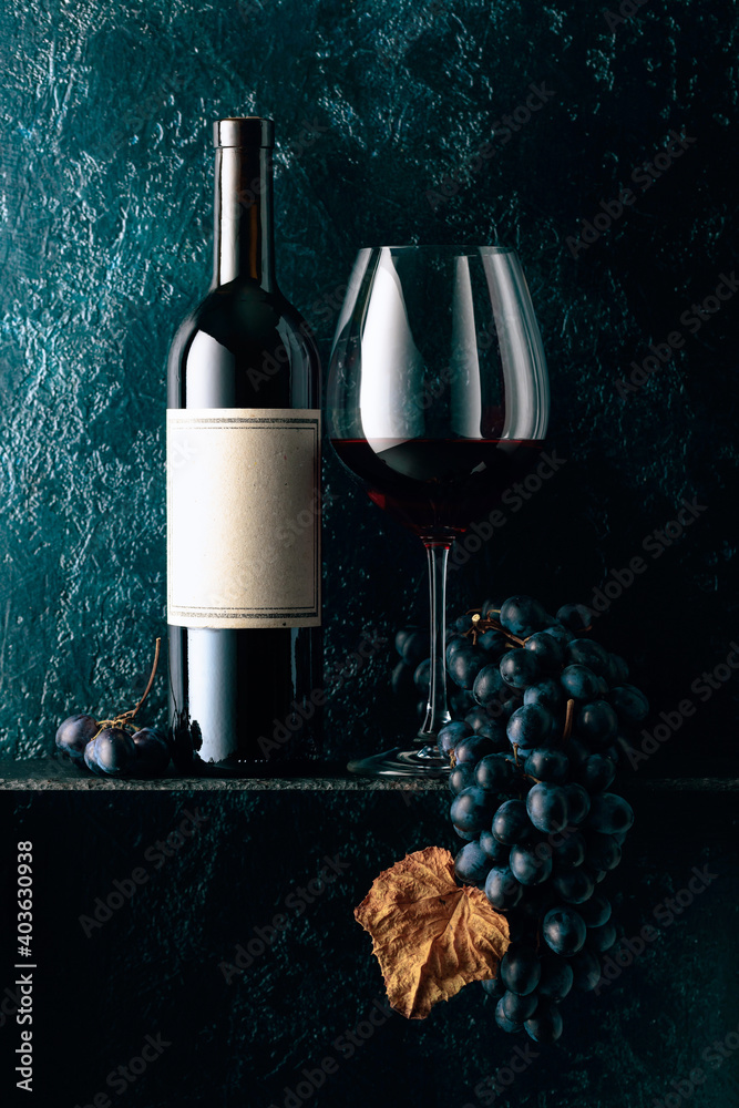 Red wine and blue grapes with dried up vine leaves on an old dark blue background. - obrazy, fototapety, plakaty 