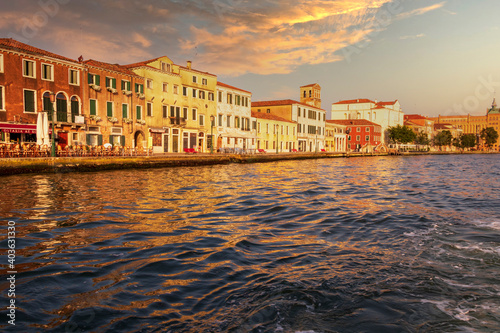 Beautiful landscape by the river of Giudecca island in front of Venice while sunset with blue river and clouds in orange color.
