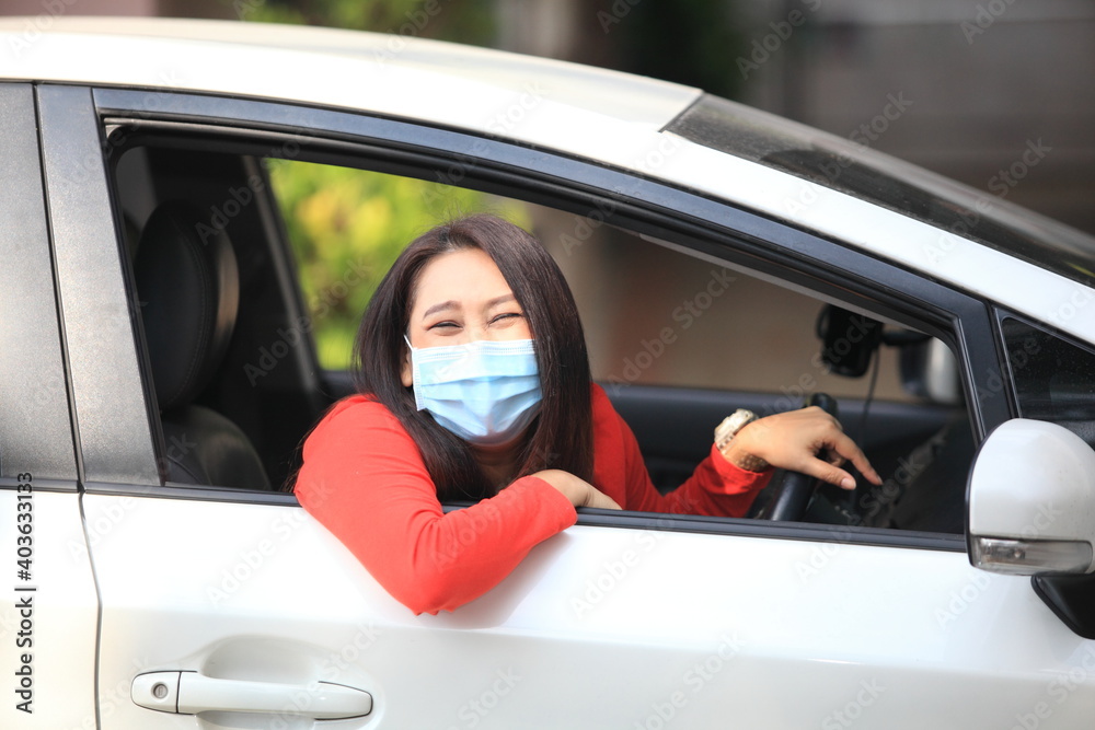  Young woman with medical protective mask on her face is driving a car, she looks into camera and View from outside , Protect yourself.
