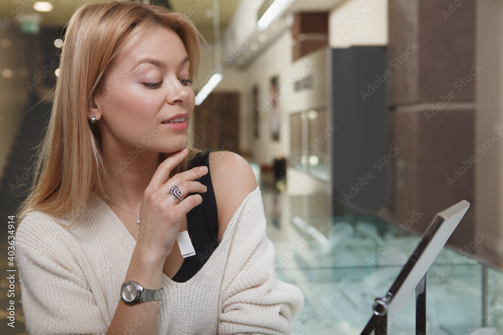 Attractive woman looking in the mirror at jewelry store, trying on jewellery Attractive woman looking in the mirror at jewelry store, trying on jewellery