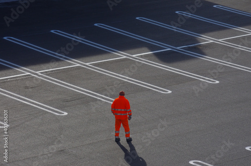 Worker in orange overalls with reflective band walks in a car-free parking lot