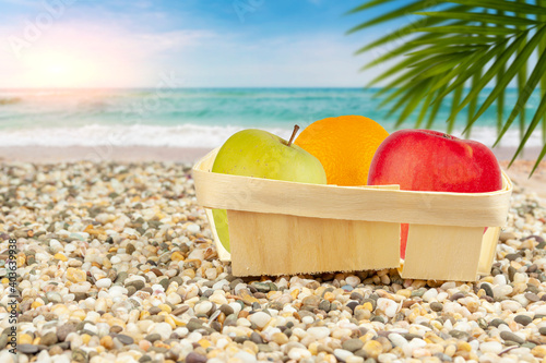 Packaged apples and oranges lie on the beach by the sea.