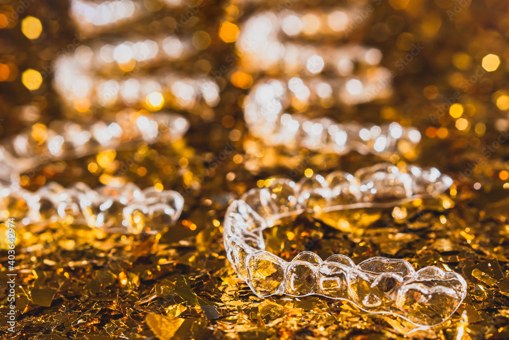 Invisible dental teeth brackets tooth aligners on gold background. Plastic braces dentistry retainers to straighten teeth. Invisible dental teeth brackets tooth aligners on gold background. Plastic braces dentistry retainers to straighten teeth.
