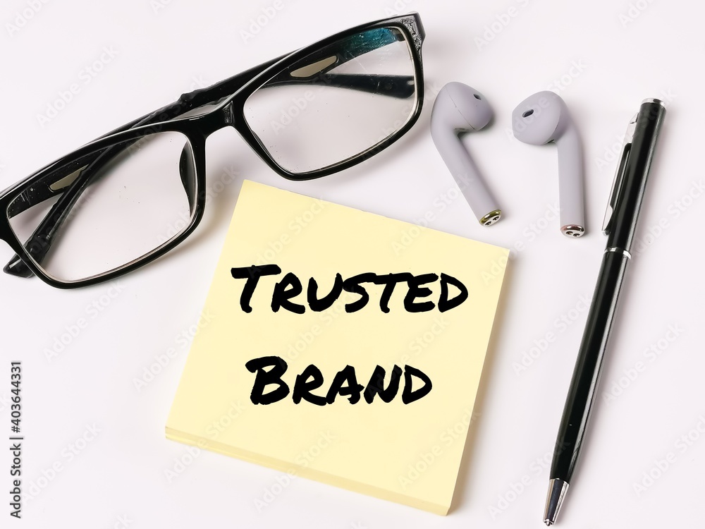 Text TRUSTED BRAND on paper note with ear phone,eye glasses and pen isolated on white background. Business concept. 