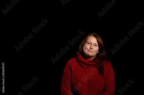 Pretty woman in a red woolen sweater posing smiling on black studio background. Copy space
