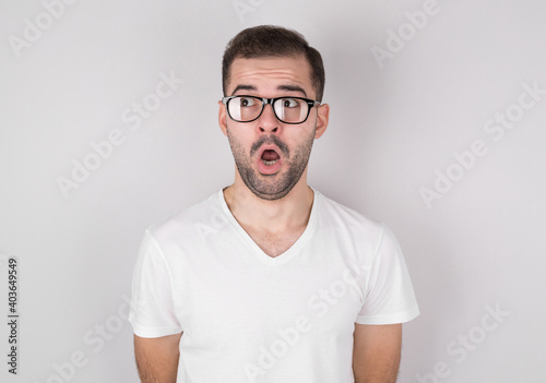 Portrait of a shocked young man looking aside over gray background.