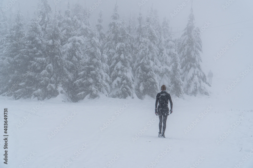 Woman walking in a snowstorm, Young woman running on the mountain in bad weather in winter. Beautiful girl jogging in blizzard or snowstorm