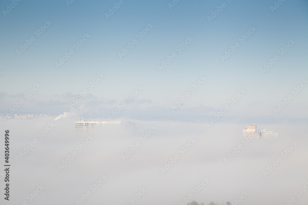 Roofs of several high rise buildings in the fog against blue sky Roofs of several high rise buildings in the fog against blue sky
