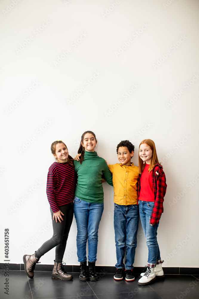 Obraz premium Portrait of cute little kids in jeans looking at camera and smiling, standing against white wall