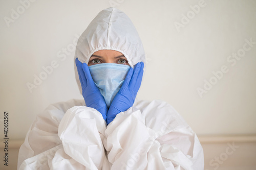 A woman in a protective suit and a medical mask in horror holds her hands to her face