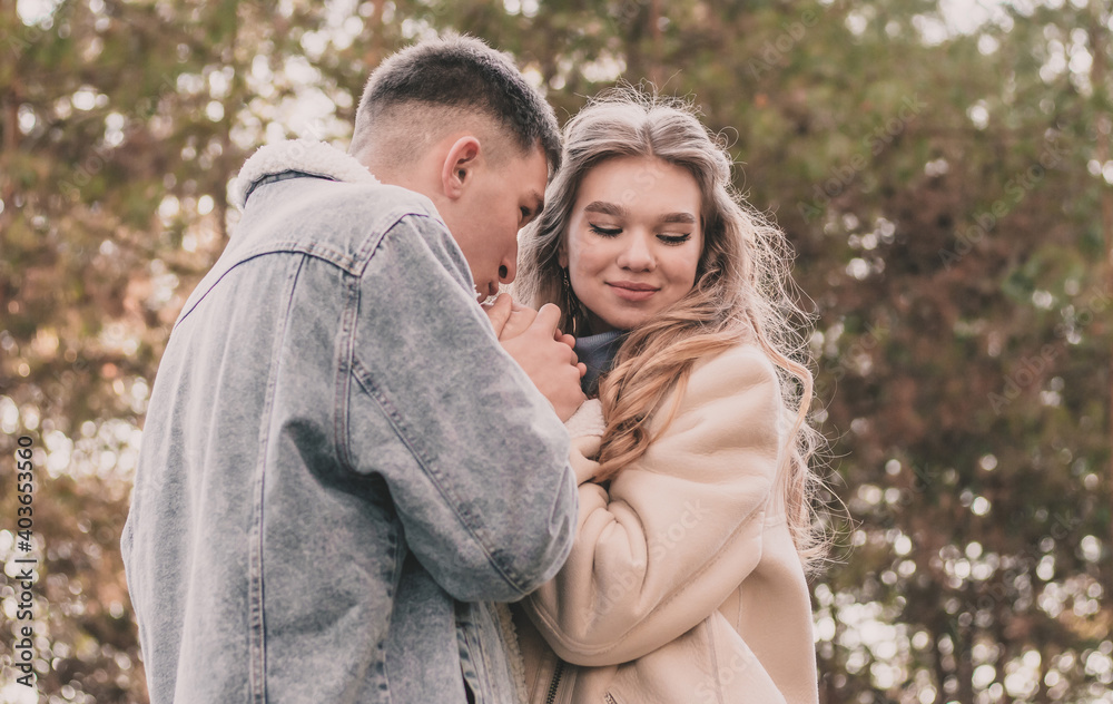 Fototapeta premium the guy holds the girl's hands and kisses them and the girl smiles while in the pine forest in winter