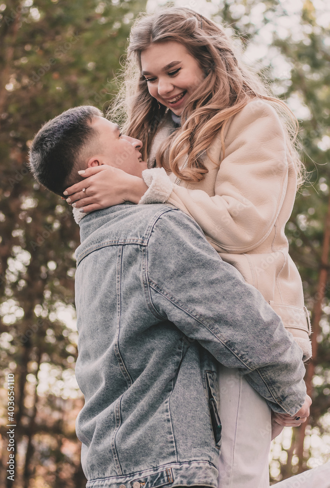 The girl jumped into the arms of the guy, holds his face with her hands and smiles in the pine forest