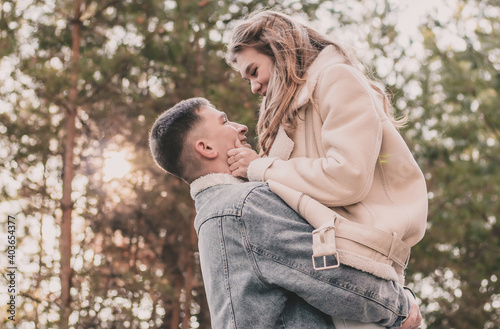 The girl jumped into the arms of the guy  holds his face with her hands and smiles in the pine forest