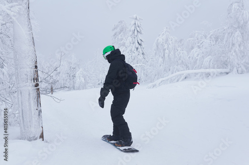 teenage snowboarder going to slide down a mountain along a forest trail in frosty weather