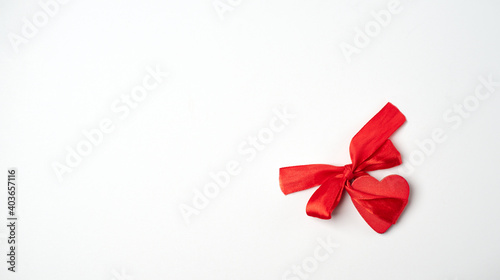 Red wooden heart with red bow-knot on the light (white) background. Valentine's Day concept. Flat lay, top view, space for text.