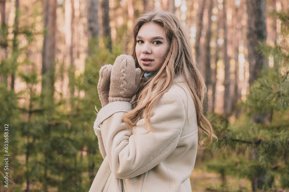 a young girl of model appearance in a pine forest is dressed in a fur coat and a warm sweater shows hands in mittens and smiles a young girl of model appearance in a pine forest is dressed in a fur coat and a warm sweater shows hands in mittens and smiles
