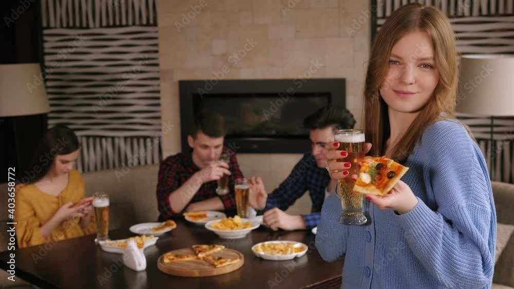 Portrait of a girl with a glass of beer and a slice of freshly baked pizza in a pizzeria, she looks at the camera and smiles. Friends enjoy pizza and beer in the cafe. Portrait of a girl with a glass of beer and a slice of freshly baked pizza in a pizzeria, she looks at the camera and smiles. Friends enjoy pizza and beer in the cafe.