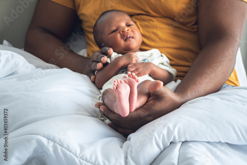 Blur soft images of An African American father holding his 12-day-old baby newborn son lying in bed in a white bedroom, concept to African American family and newborn