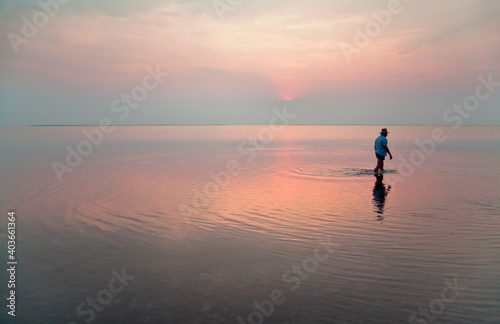 Lake Syvash at sunset,  a man walking in the reflection of the pink sky. © Uilia