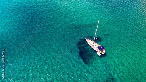 Yacht anchoring in crystal clear turquoise water in front of the tropical island, alternative lifestyle, living on a boat. Aerial view of yacht at anchor on turquoise water, showing luxury, wealth. © daliu
