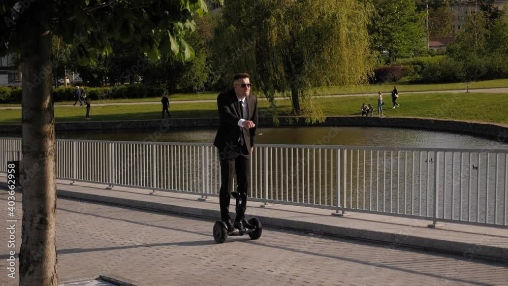 A cheerful man in a suit rides a gyro scooter in the Park, he has fun and simulates a slow run. A happy businessman is having fun with a gyro scooter. Slow motion.