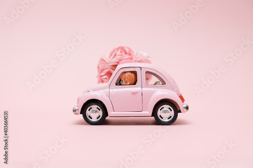 Pink retro toy car delivering bouquet of flowers box on pink background. February 14 card, Valentines day. Flower delivery. 8 March, International Happy Womens Day.