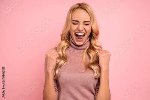 Portrait of beautiful joyous woman screaming and gesturing as winner isolated over pink background in studio