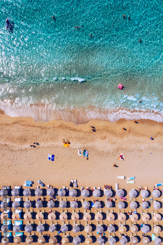 Aerial view of sandy beach with colorful umbrellas, swimming people in sea bay with transparent blue water at sunset in summer. Aerial top view on the beach, umbrellas, sand and sea waves.