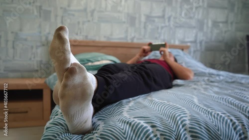 a man in dirty socks lies on the bed and uses the phone