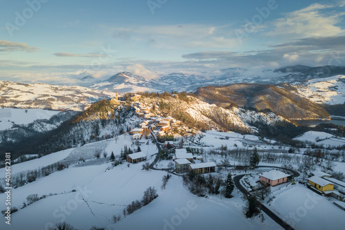 Aerial panoramic view of Ruino town in Oltrepo Pavese covered in snow at sunset