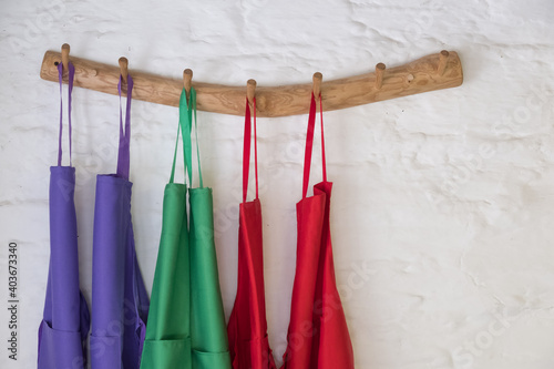 Coloured cooking aprons hung up on wooden pegs