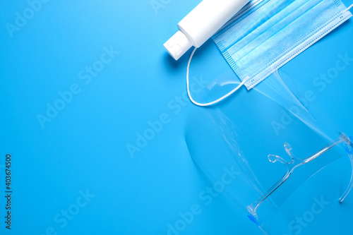 A picture of face shield, mask and hand sanitizer on copyspace blue background.