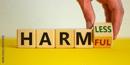 From harmful to harmless. Male hand turns the cube and changes word 'harmful' to 'harmless'. Beautiful yellow table, white background. Business and harmful or harmless concept. Copy space. photo