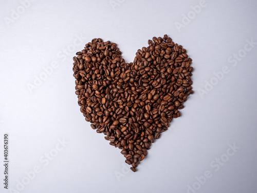 A large brown heart made of coffee beans lies on a bright white paper