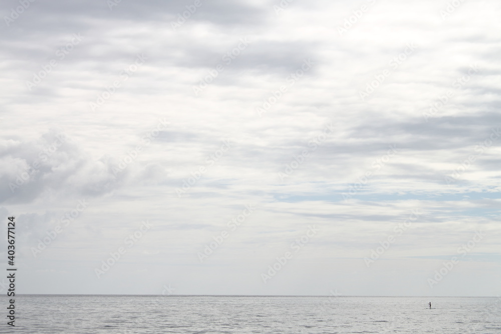 sea scene, lonely person paddle surfing in the ocean far from shore, a minimalist panoramic point of view of a cloudy sky
