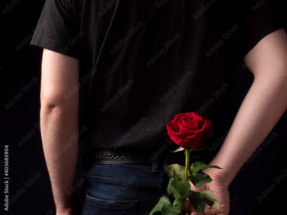 Young guy in a black t-shirt suit holds a red rose behind him
