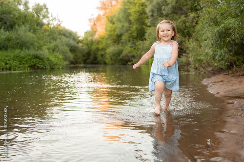 Fototapeta Naklejka Na Ścianę i Meble -  a little girl runs in the river in shallow water along the shore. She laughs and has fun