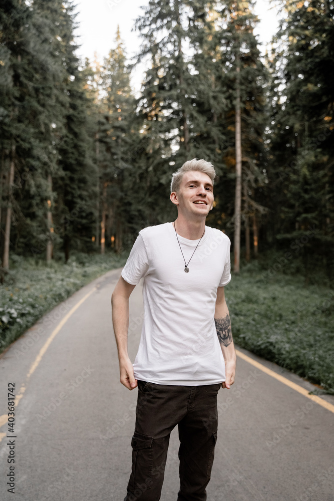 an unusual guy with gray hair stands in the middle of the forest smiling