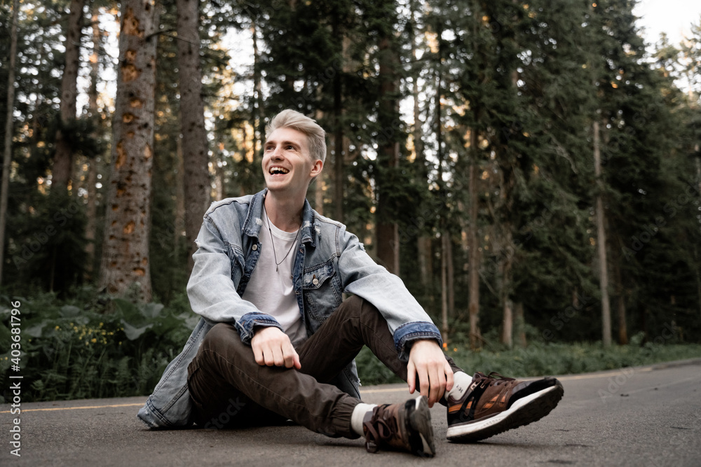 Obraz premium an unusual young guy with gray hair sits on the ground and laughs out loud