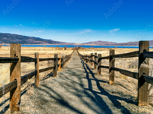 Fenced pathway into a wildlife refuge with a lake and mountains in the background.