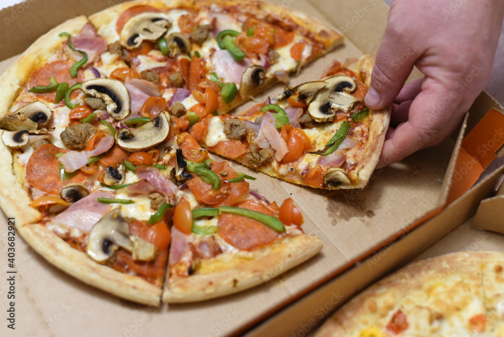 A hand pulls a slice of delicious hot freshly made pizza out of the box. A hand pulls a slice of delicious hot freshly made pizza out of the box.