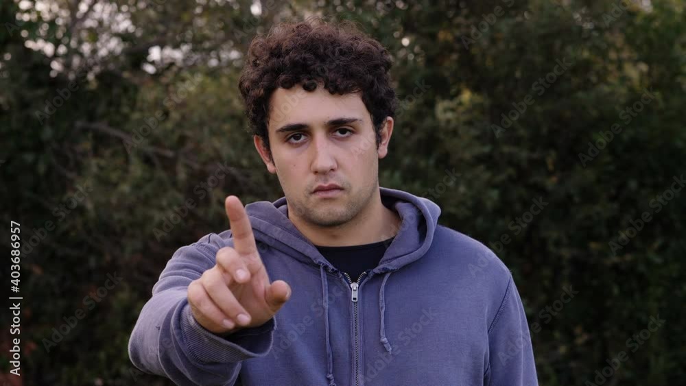 forbid, negation - young man at park makes no with his finger to the camera forbid, negation - young man at park makes no with his finger to the camera