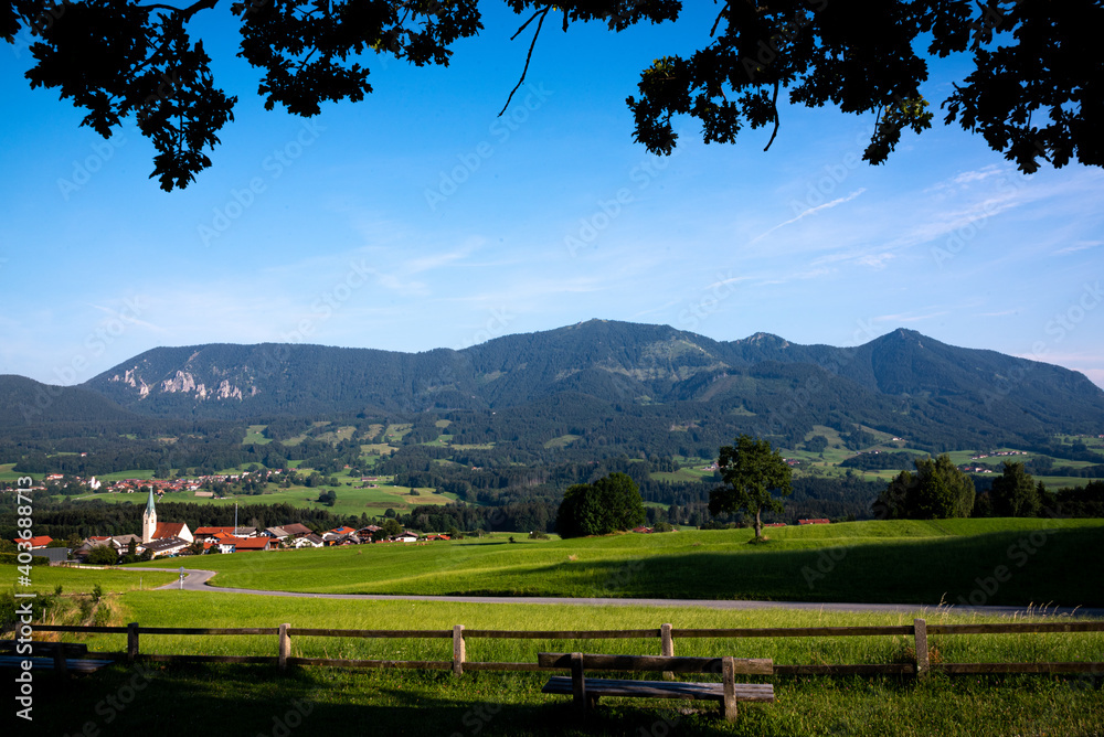 A beautiful view of a small bavarian village in the foothills of the Alps, green rolling hills and blue sky - Bavarian Alps, Rosenheim, Bavaria, Germany

