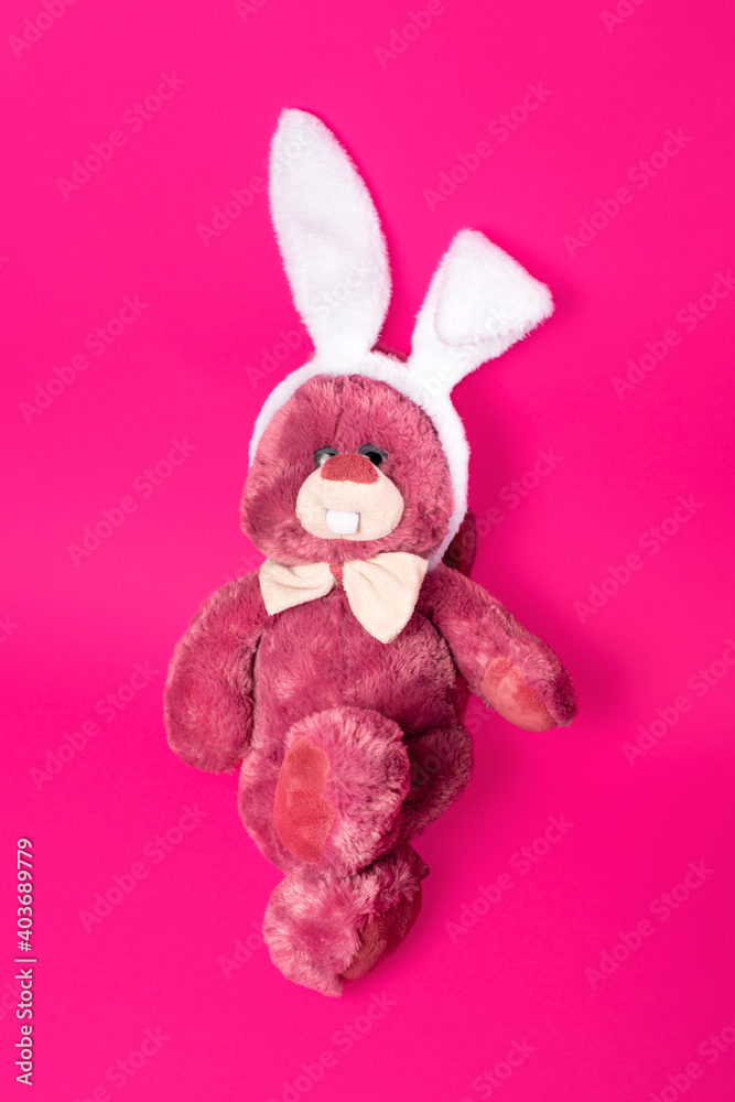 Funny and fluffy toy pink bunny in white fluffy bunny ears hoop isolated on pink background
